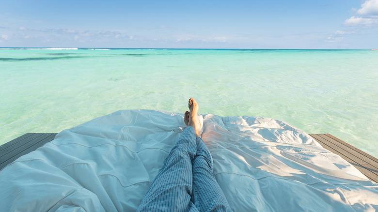 two legs in pajamas on a bed on the edge of a clear sea