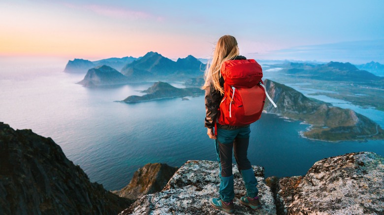 A female hiker stands atop a mountain overlooking the sea and islands