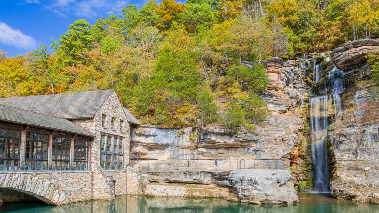 Stone building flanking forested cliffs with a waterfall flowing down into a pool at Dogwood Canyon Nature Park in Missouri