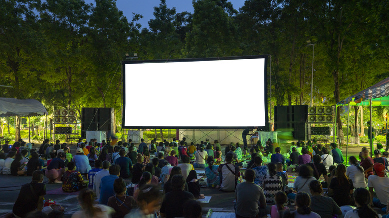 An audience gathers in front of a movie screen in the woods