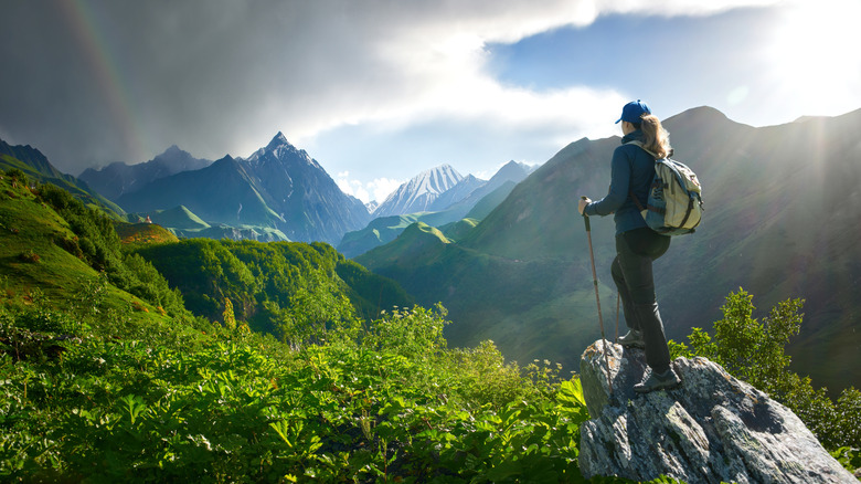 A woman hiking in the country of Georgia with mountains and a rainbow in the background