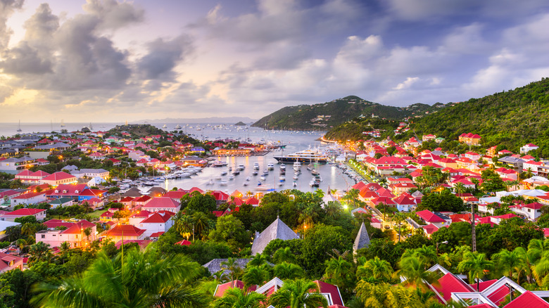 Yachts bobbing in St. Barts' harbor during golden hour, surrounded by houses with red roofs
