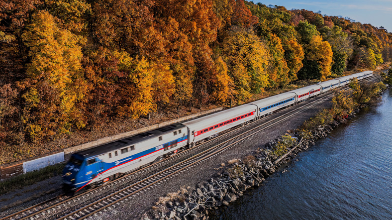 An aerial view of Amtrak train passing by, taken from over the Hudson River on a sunny day in autumn.