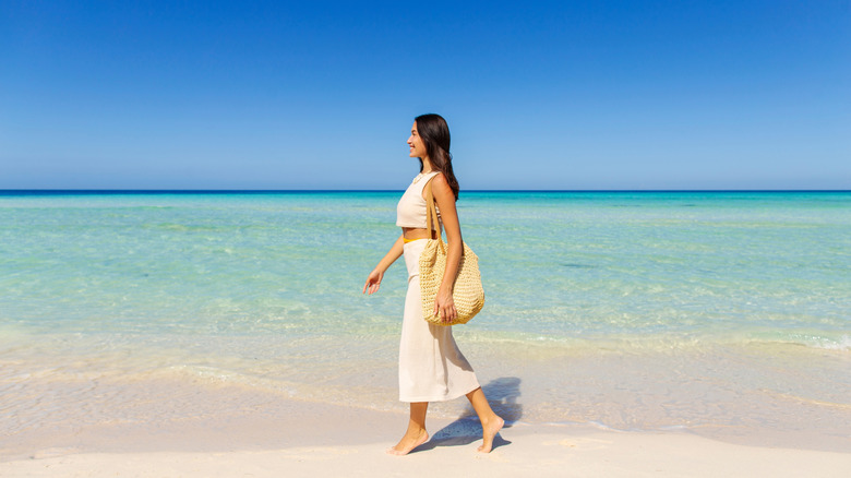 woman with a bag side view walking on sandy beach at islands