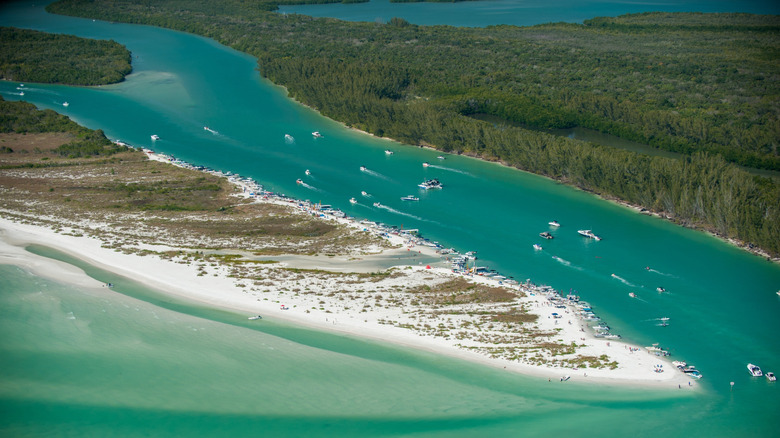 Boats in a channel between a beachy barrier island and mangrove swamps