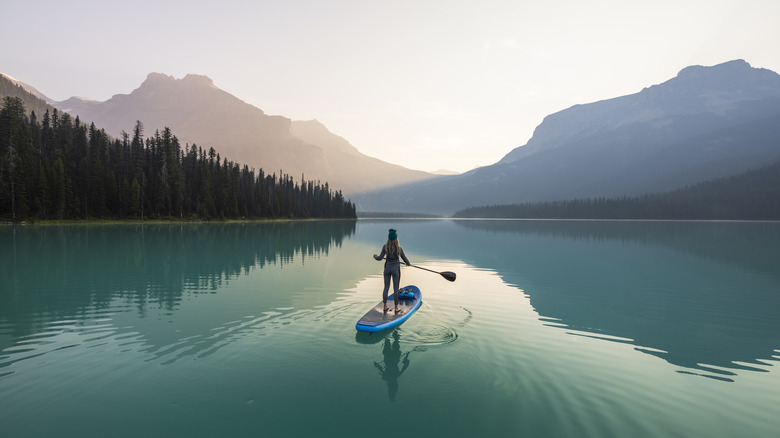 A woman paddle boarding on a pristine lake with mountains in the background