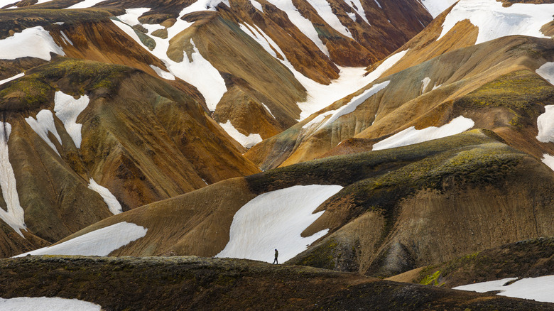 A person in the distance walking amid snow-capped peaks