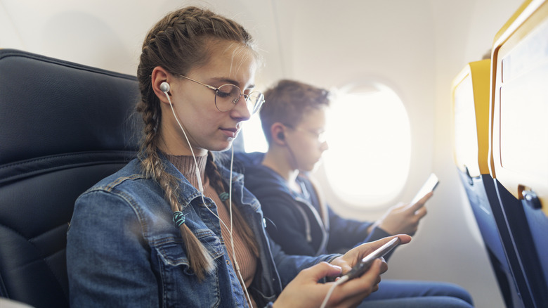 Teens using headphones on a plane.