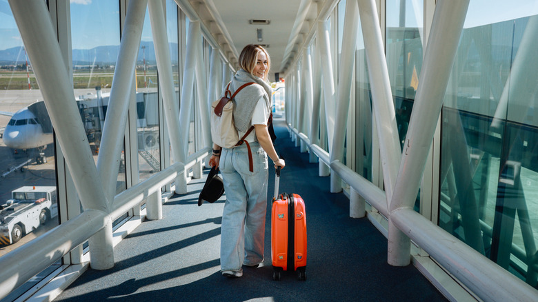 Woman walking down air bridge with rolling suitcase