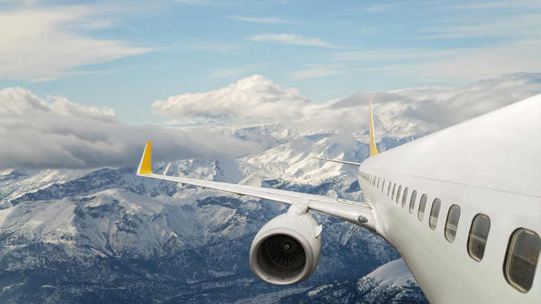 A plane flying above snowy mountain peaks and clouds