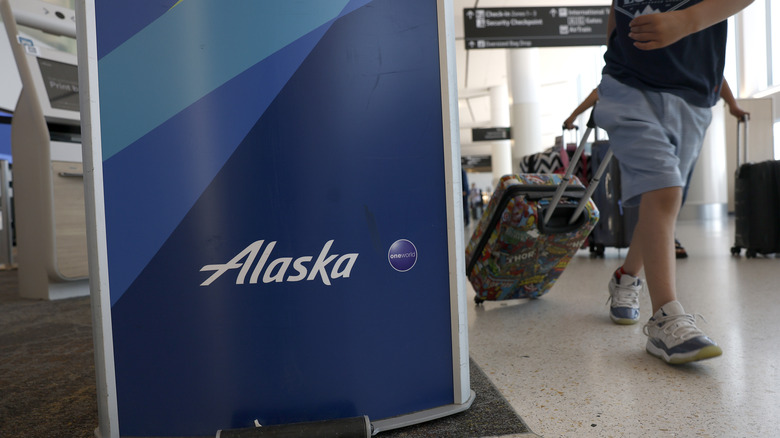 Alaska Airlines signage and a passenger walking by with luggage