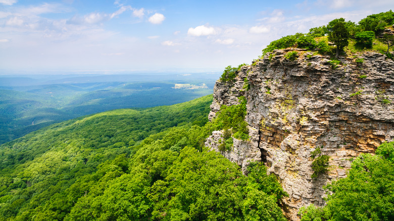 A rocky cliffside on a mountain with aerial views of a forest