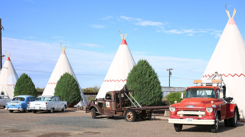 large conical structures around a concrete lot with vintage cars, blue sky