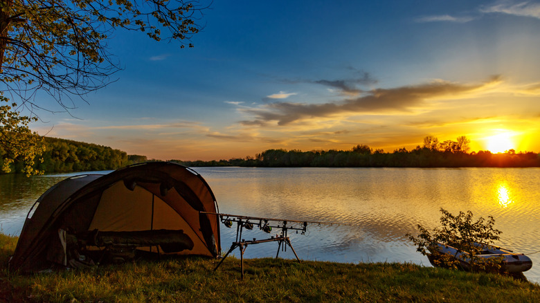 tent and fishing poles lakeside with boat at sunset