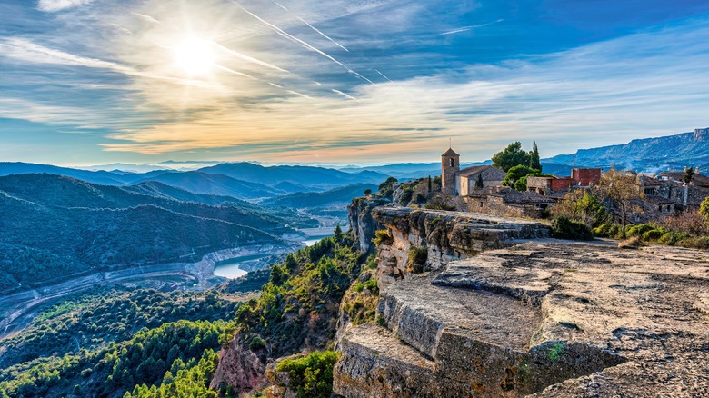 A small village church on a rocky cliff with mountains in the background