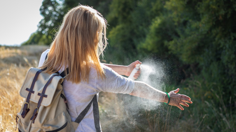 A hiker applies bug and tick spray to her arm.