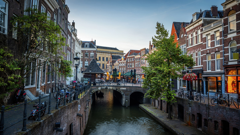 Buildings and shops along a canal and stone bridge in Utrecht, Netherlands, at dusk.