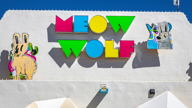 A white building in Santa Fe with a multicolored Meow Wolf sign and cartoon animals.