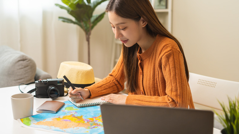 woman writing on a notepad, laptop, map, camera