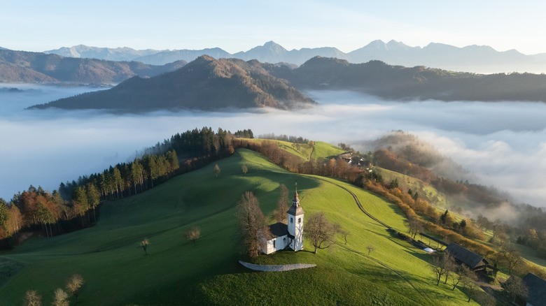 Picturesque small church on the top of a hill with foggy mountains in backdrop, Slovenia