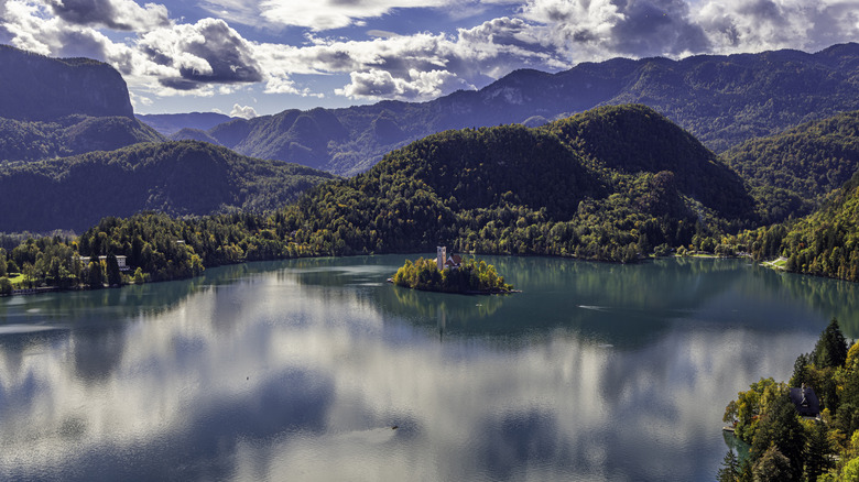 Clouds over forested mountains in the background with Lake Bled and its island in the foreground