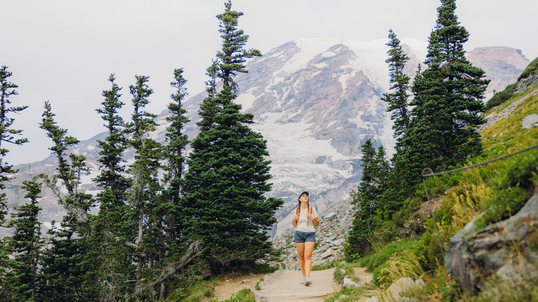 Front view of active sport female with backpack hiking through scenic footpath with background view of mount Rainier and glacier during summertime