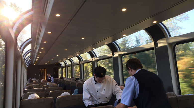 Chef and waiter serving food in a luxury train car with huge glass windows