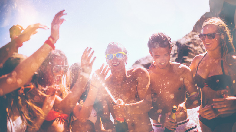 young adults popping champagne at the beach partying