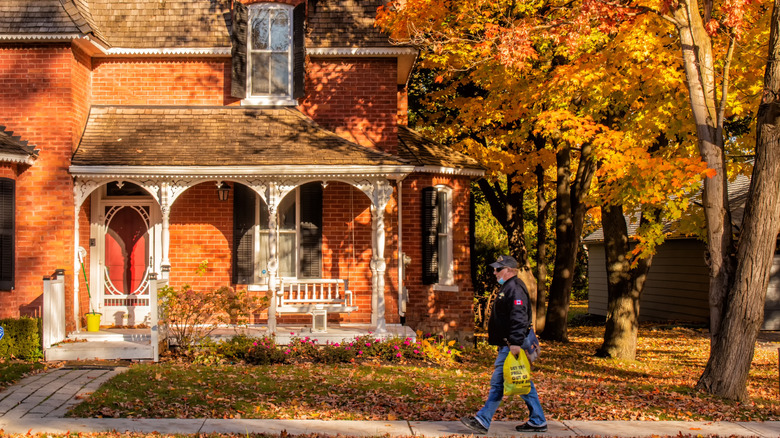 A man walking on the sidewalk with fall foliage on trees