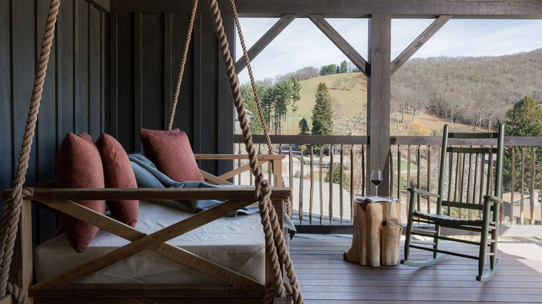 A padded swinging bench on a patio with a rocking chair overlooking the grounds from a suite at Cataloochee Ranch's Silverbell Lodge in Maggie Valley, North Carolina.