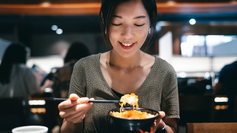 A Japanese woman lifts her bowl from the table at a restaurant