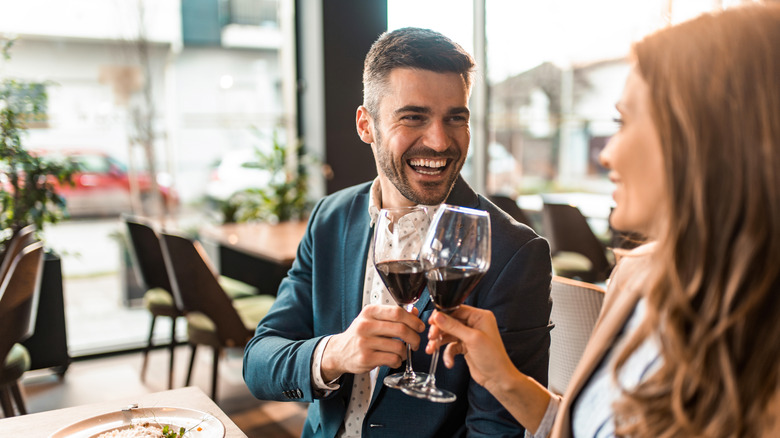 Happy young man toasting with wine while having lunch with his girlfriend in a restaurant