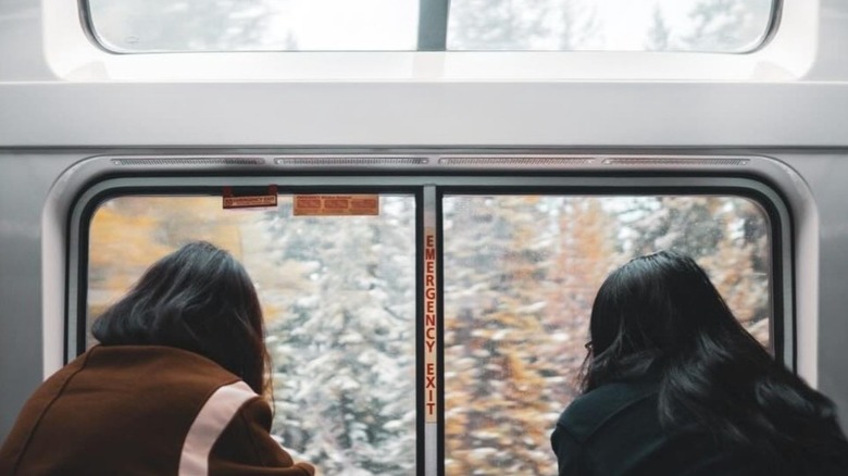 Two female train passengers looking out the window at a snowy forest