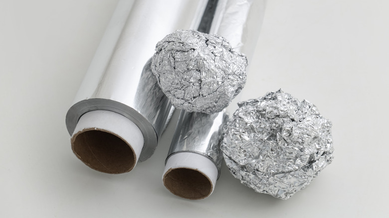 Rolls and balls of aluminum foil lie on a blank surface