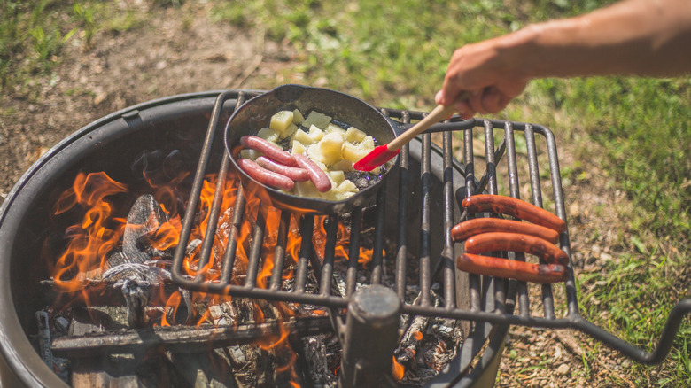 A camper barbecues over an open fire