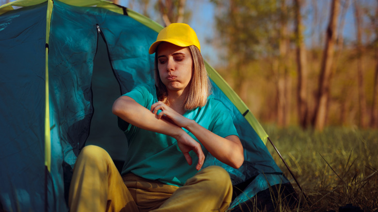 A woman scratching her bug bites at a campsite.