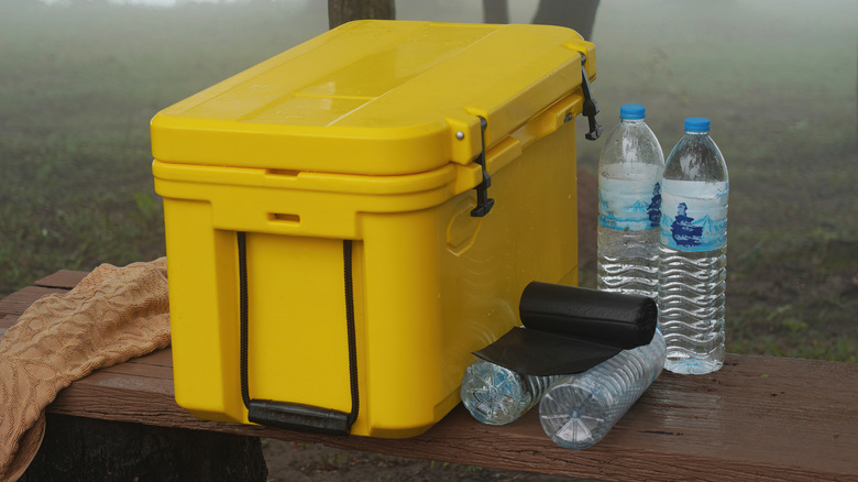 A yellow cooler on a wooden bench with water bottles beside it