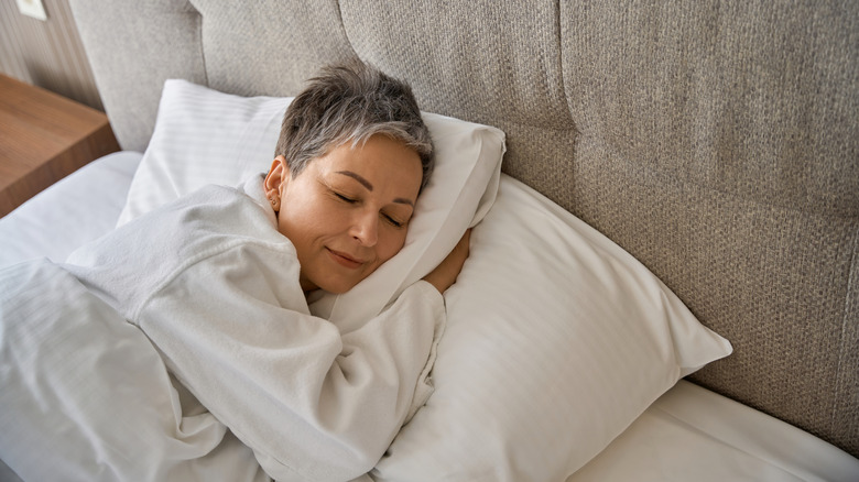 A woman smiling while sleeping in a hotel bed.