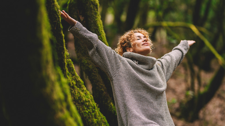 A woman stretches her arms contentedly in a wooded setting