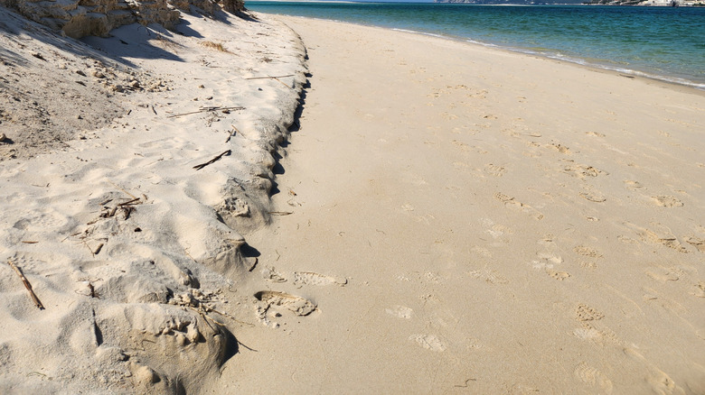 A beach with white sand and cliffs in the distance