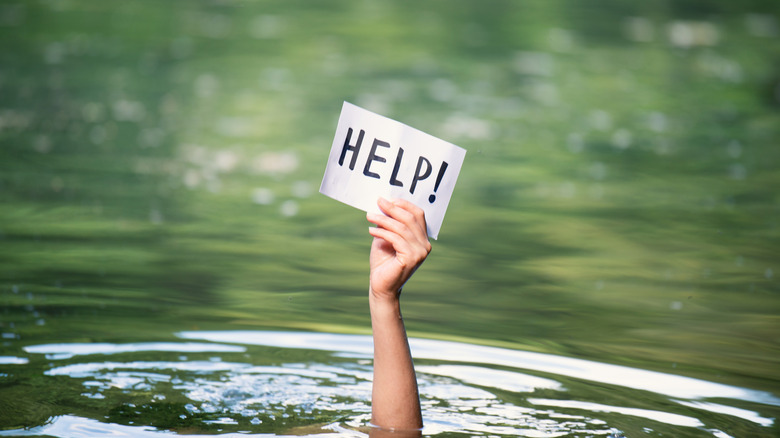 Person drowning holds a sign out of water reading help