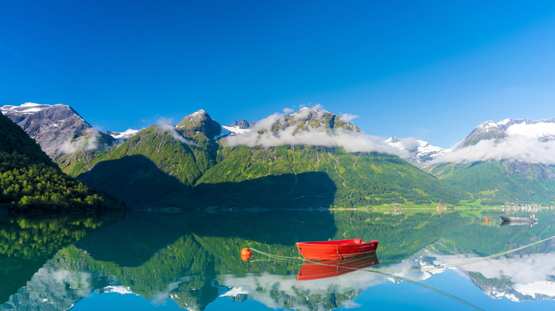 A red rowboat on a reflective lake in front of green mountains