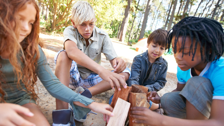 Group of camp kids work together to build a fire