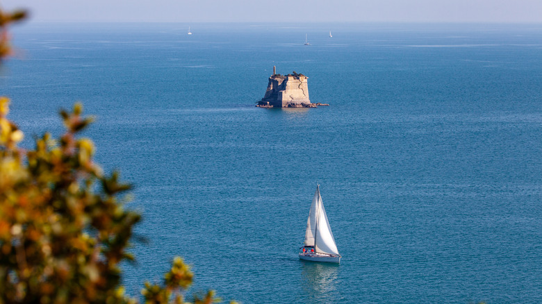 A sailboat in the water with a stone tower in the sea
