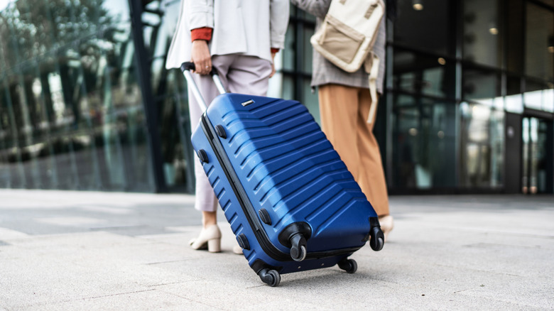 A woman dragging a blue luggage on streets