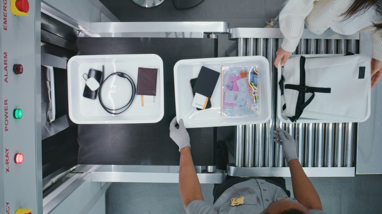 TSA agent looking over trays going into scanner