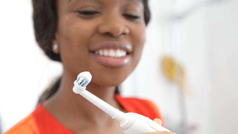 Smiling African American woman looking at electric toothbrush