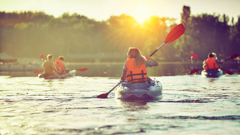 A group of friends kayaking a large river at sunset