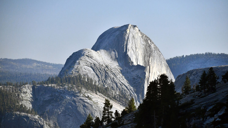 view from Olmstead Point of Half Dome jutting into the sky, with surrounding forest and mountains