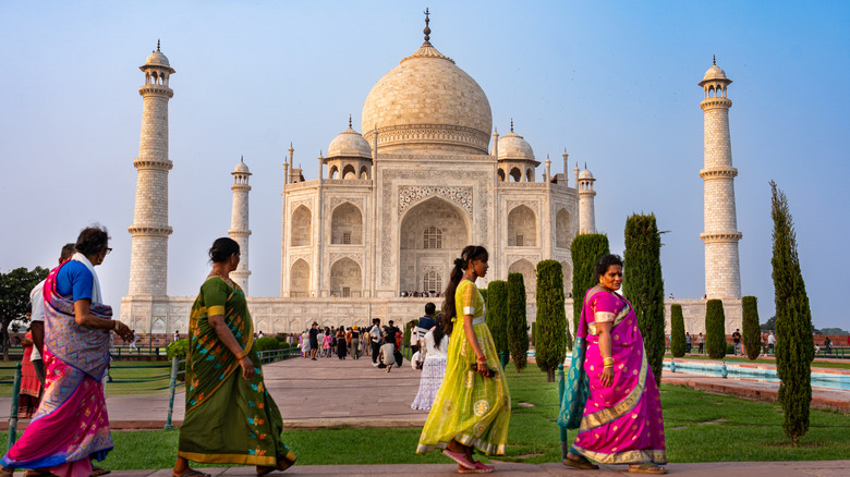 A queue of women in colorful saris walks past the Taj Mahal
